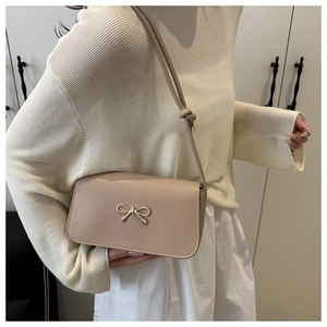 Close-up of beige crossbody bag with a delicate gold metal bow and smooth PU texture