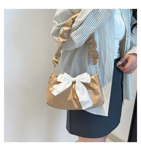 Detail of khaki pleated underarm bag featuring a large white satin bow and ruffled strap