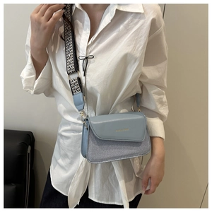 Detail of light blue crossbody bag featuring a wide geometric pattern strap and gold text