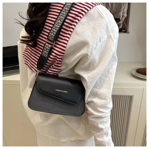 Detail of crossbody bag with black leather flap, gray fabric body, and wide woven strap