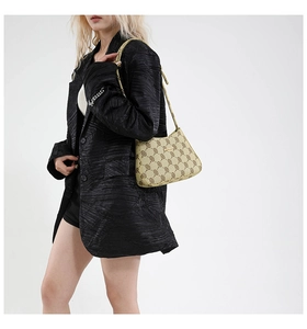 Vista laterale della borsa a spalla beige monogramma su modella con placca dorata