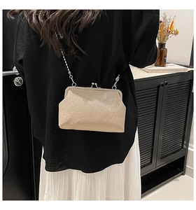 Detailed view of a gold sequin crossbody bag with a classic metal kiss lock and slim chain