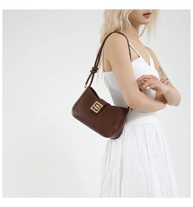Close-up of brown leather shoulder bag with a polished gold geometric metal buckle