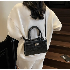 Detail of a black crocodile-patterned crossbody bag worn by a model on a wooden staircase