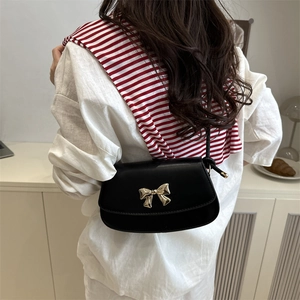 Minimalist black leather crossbody bag with golden bow clasp shown on a shoulder