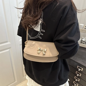 Chic beige crossbody bag with golden bow buckle on black and white outfit