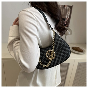 Detail of black underarm bag with gold M logo and chain strap on a white background