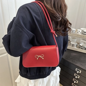 Sac à bandoulière élégant en cuir rouge pour femme avec nœud doré porté par un mannequin