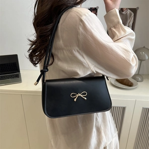 Minimalist black leather underarm bag with gold metal bow shown in a lifestyle setting