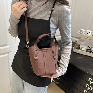 Brown lychee leather bucket bag with silver hardware shown on a shoulder model