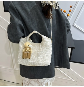 Detail of white pleated bucket bag with teddy bear charm and adjustable crossbody strap