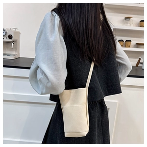 Detail einer cremeweißen Handytasche mit Litschi-Muster und Lederriemen am Modell