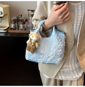 Detail of light blue pleated bucket bag with plush bear charm in a cafe setting