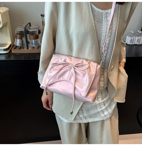 Close-up of pink satin crossbody bag with large bow detail and pleated texture design