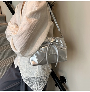 Silver bow shoulder bag with metallic finish shown on model in a stylish urban setting