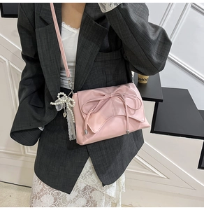 Détail du sac bandoulière rose à nœud avec pendentif perle sur une tenue de blazer