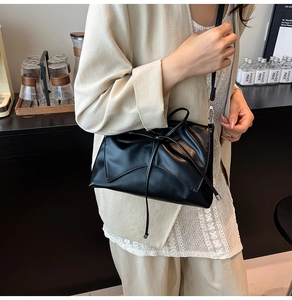 Detail of black leather crossbody bag with a decorative bow and thin strap on a model