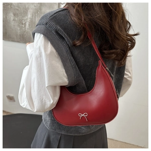Vue latérale d'un sac baguette rouge en cuir avec nœud argenté porté par un mannequin