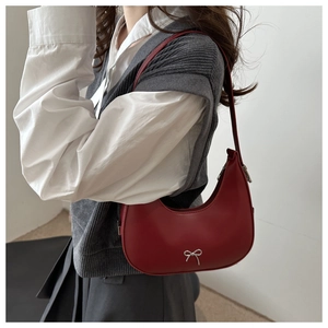 Detail of red crescent underarm bag featuring a silver metal bow accent and smooth leather