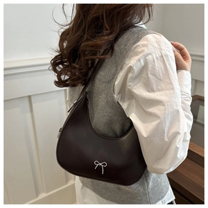 Close-up of brown crescent underarm bag with silver metallic bow detail on PU leather