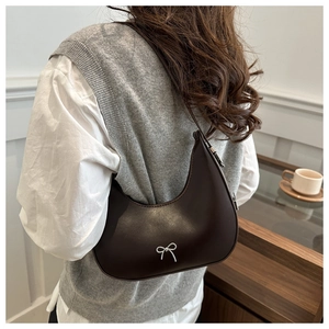 Detail view of a coffee brown crescent hobo bag with a silver bow and smooth leather texture