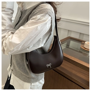 Detail of dark brown leather hobo bag with a silver bow decoration on model shoulder