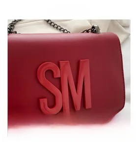 Close-up of vibrant red leather crossbody bag featuring a large 3D logo and black metal chain