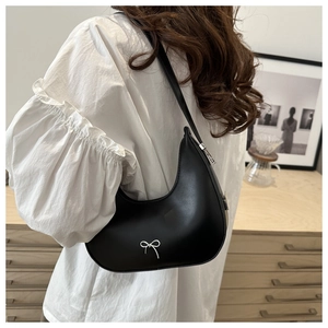 Side view of black hobo bag with silver bow detail worn by model in a cozy indoor setting