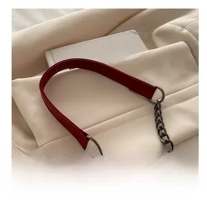 Close-up of red leather and gunmetal chain shoulder strap on beige fabric