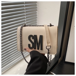 Detail of cream crossbody bag with prominent black SM letters and silver chain strap