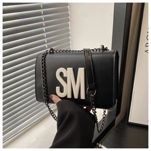 Detail of black faux leather bag featuring bold 3D white letters and a metal chain strap