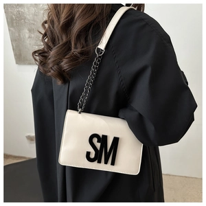 Detail view of cream flap crossbody bag with bold SM logo and metal chain strap