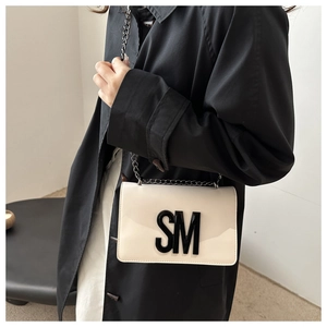 Detail of cream glossy leather square bag featuring a bold black SM logo and metal chain