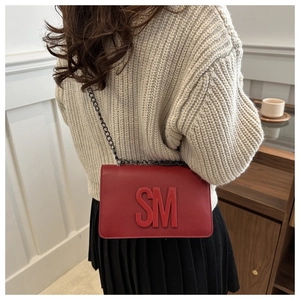Red flap shoulder bag with 3D SM logo and black metal chain worn by a model