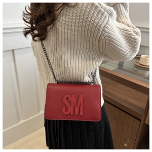 Red flap bag with gold SM letters and chain strap worn by model in casual setting