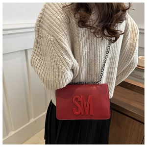 Close-up of red leather shoulder bag with SM logo and dark grey metal chain strap