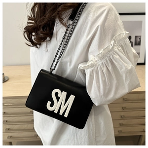 Close-up of stylish black shoulder bag with large white SM letters and metal chain strap