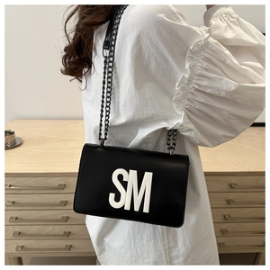Detail of black leather crossbody bag with white SM letter logo and dark metal chain