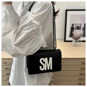 Detail of black crossbody bag featuring large 3D SM letter logo and dark metal chain strap