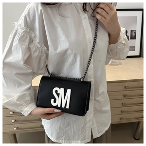 Detail view of the black crossbody bag with white SM lettering and metal chain strap