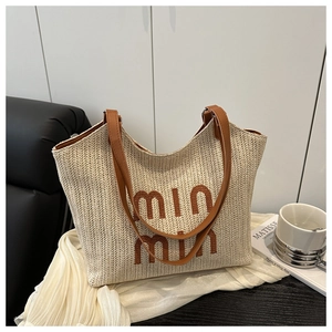 Detail of off-white straw tote bag featuring brown 3D embroidered text and leather straps