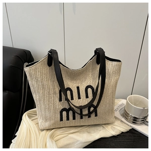 Detail of embroidered logo on a beige woven straw tote bag with black leather handles