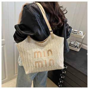Detail view of woven straw tote bag featuring embroidered letters and long leather strap