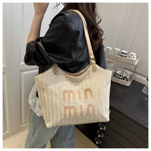 Detail of beige woven straw tote bag with min min embroidery and leather handles