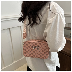 Detail of a pink crossbody camera bag with M-pattern print and wide geometric shoulder strap