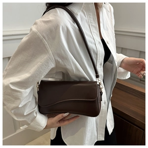 Close-up of deep brown leather baguette bag with gold metal hooks and white shirt contrast