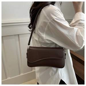 Detail of a dark brown rectangular shoulder bag with a unique wavy curve flap design