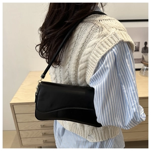 Detail of a minimalist black leather shoulder bag styled on a model for a modern look