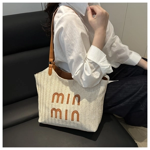 Detail of woven straw tote bag featuring brown leather straps and embroidered letters