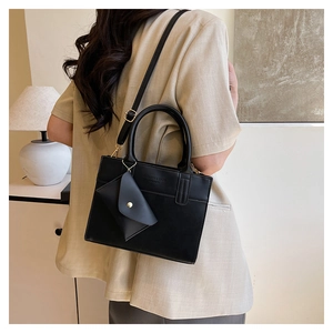 Detail of black leather handbag featuring adjustable strap and triangular charm on model